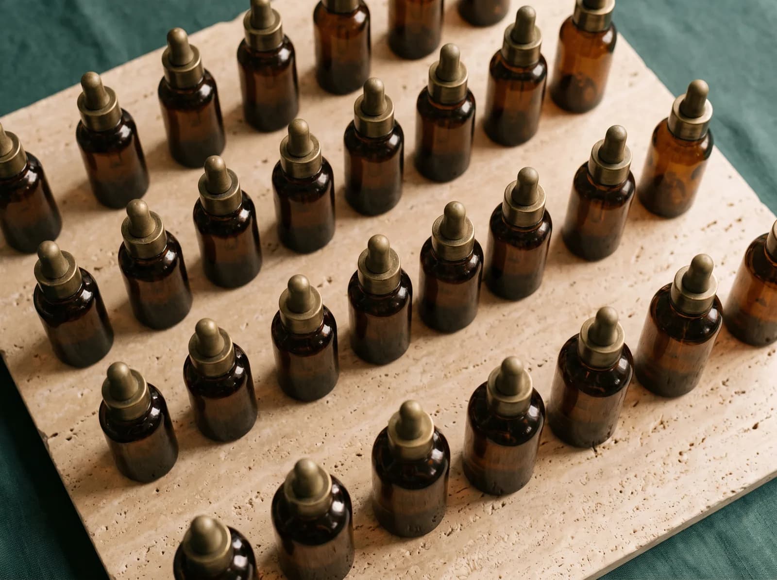An ordered overhead grid of identical amber serum bottles on warm travertine — volume and consistency in one frame.